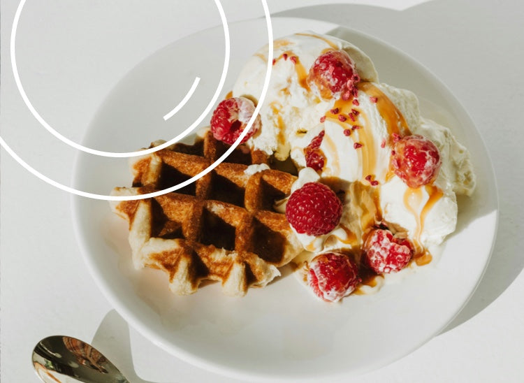 A breakfast waffle with 2 scoops of vanilla ice cream, fresh raspberries and a toffee sauce topping