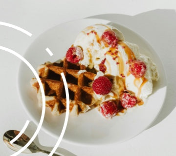 A breakfast waffle with 2 scoops of vanilla ice cream, fresh raspberries and a toffee sauce topping